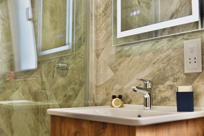 A bathroom with a marble wall, a mirror, a sink, and a shower. - Alight Sauna and SPA Penthouse (Xewkija)