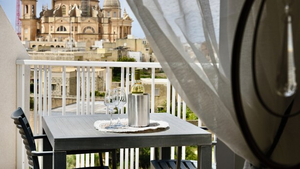 A balcony with a table, two wine glasses, and a bottle of wine. - Alight Sauna and SPA Penthouse (Xewkija)