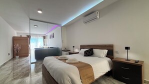 A modern hotel room with a large bed, bedside tables, a nightstand, and a built-in air conditioning unit. - Alight Sauna and SPA Penthouse (Xewkija)