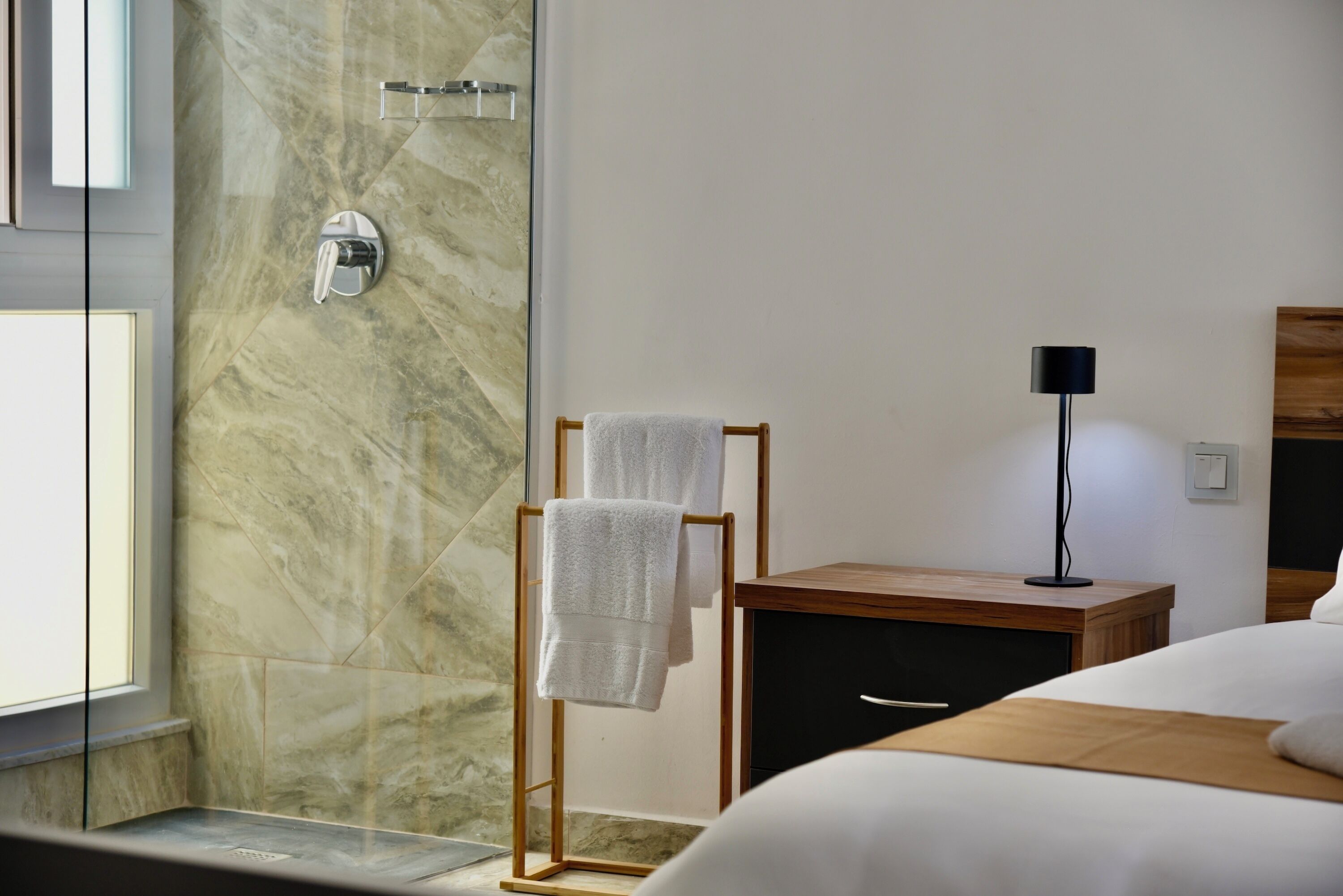 Una habitación de hotel moderna con ducha, mesita de noche de madera, lámpara y cama.