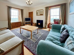 A living room with a sofa, a coffee table, a television, a fireplace, and a window with curtains.