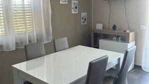 A modern dining area with a white table and chairs, a flat-screen TV mounted on the wall, and framed artwork on the wall. - Panorama d'oro (Sicilia)