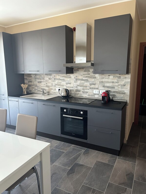 A modern kitchen with grey cabinets, a built-in oven, and a stone backsplash. - Panorama d'oro (Sicilia)