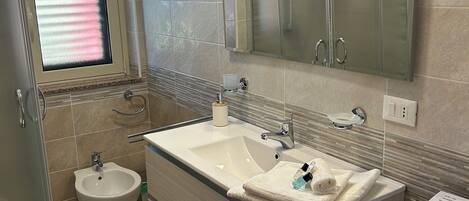 A modern bathroom with a large sink, a bidet, a toilet, and a glass shower enclosure.