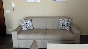 A neutral-toned living room with a beige sofa, two patterned throw pillows, and abstract wall art. - Panorama d'oro (Sicilia)