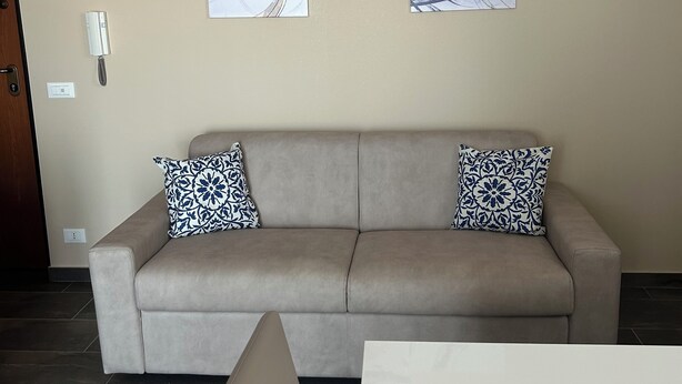 A neutral-toned living room with a beige sofa, two patterned throw pillows, and abstract wall art. - Panorama d'oro (Sicilia)
