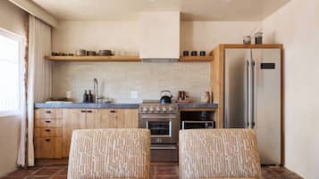 Una cocina moderna con armarios de madera, un refrigerador de acero inoxidable y un horno empotrado. Hay dos sillas con diseño en el área de descanso.