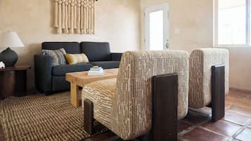 Una sala de estar con un sofá, dos sillones estampados, una mesa de centro de madera, una lámpara y una alfombra tejida.