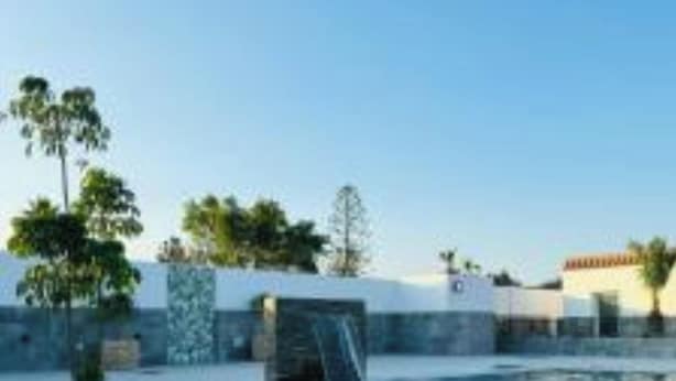 A swimming pool with clear blue water, surrounded by a low stone wall and a few trees. - Far from nothing and close to everything.  (AN)