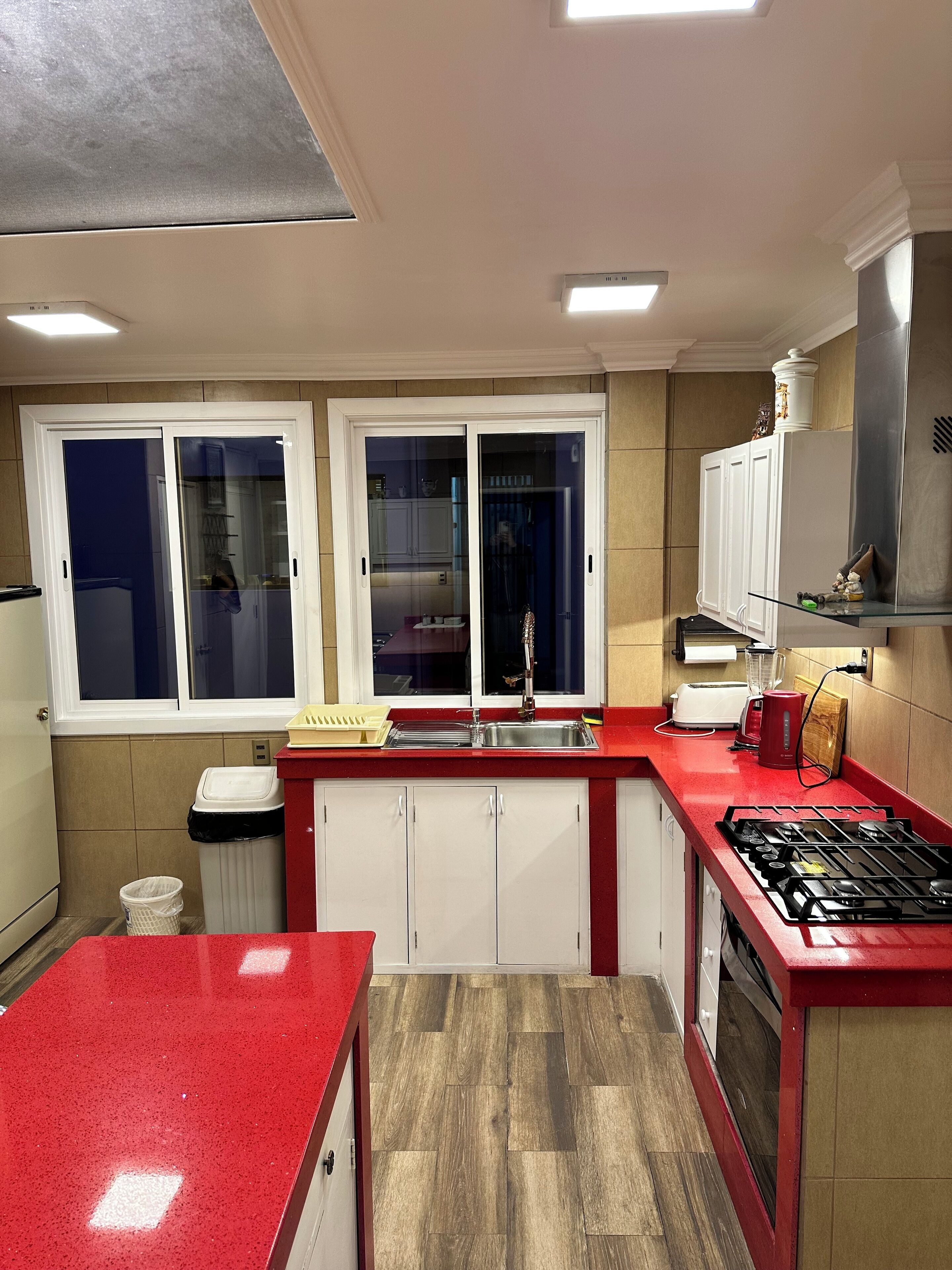 A kitchen with a red countertop, white cabinets, a stainless steel sink, and a gas stove.
