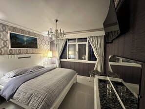 Camera da letto con un letto, comodino, lampada, finestra con tende e un lampadario.