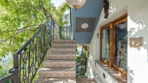 Un escalier orné de rampes travaillées et de marches à motifs, menant à une pièce dotée d’une grande fenêtre et d’un lustre décoratif au plafond.