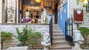 Une façade d’immeuble ornée de statues classiques, une porte bleue et une enseigne indiquant « Casa Roma ».