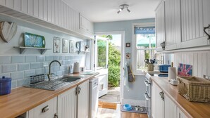 Une cuisine avec des meubles blancs, un plan de travail en bois et une vue sur le jardin grâce à une porte ouverte.