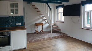 A kitchen with white cabinets, a wooden table, and a staircase leading to a landing. - Lovingly renovated East Frisian brick house "Huus up Hook" (Krummhörn)