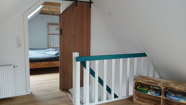 A bedroom with a wooden bed, a white radiator, and a wooden shelf with children's toys. - Lovingly renovated East Frisian brick house "Huus up Hook" (Krummhörn)