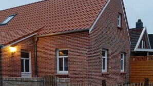 A brick building with a red-tiled roof, a wooden fence, and a paved walkway. - Lovingly renovated East Frisian brick house "Huus up Hook" (Krummhörn)