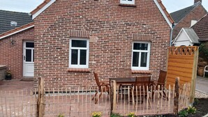 A brick house with a triangular roof, two windows, and a wooden fence with a table and chairs outside. - Lovingly renovated East Frisian brick house "Huus up Hook" (Krummhörn)
