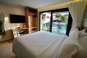 A hotel room with a large bed, a desk, a wardrobe, and a balcony with a view of the outside.
