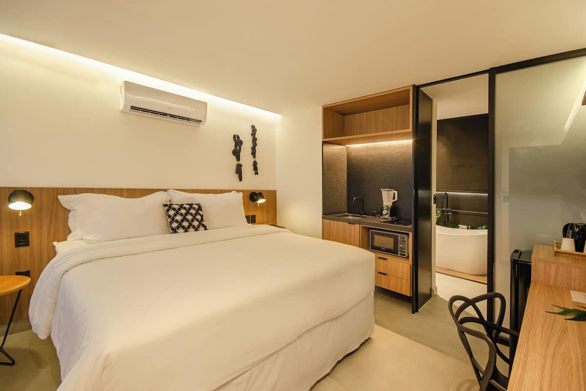A modern hotel room with a large bed, bedside tables, a built-in desk, and a shower area.