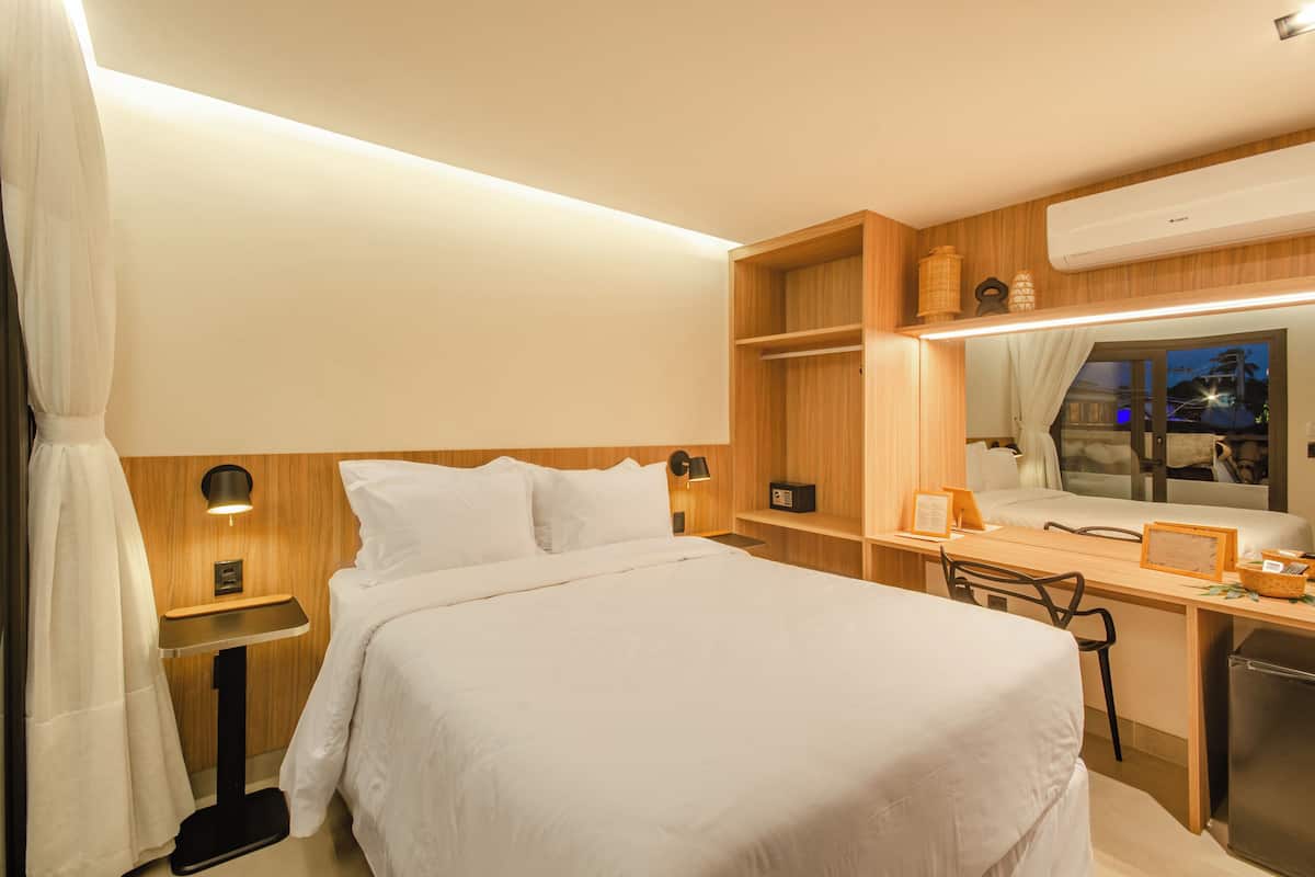 A hotel room with a bed, bedside table, lamp, desk, chair, and a mirror.