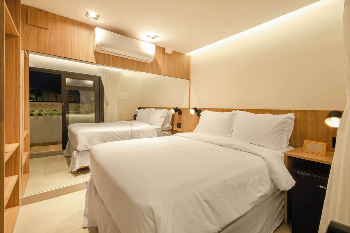 A hotel room with two beds, a wooden headboard, a nightstand, a mirror, and an air conditioning unit.