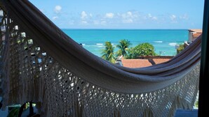Blick von einer Hängematte auf einen Strand mit klarem Himmel und Palmen.