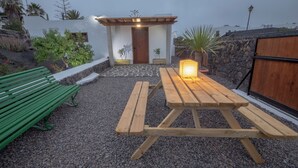 Un espace patio avec une table et un banc en bois, entouré de gravier et de plantes en pot.