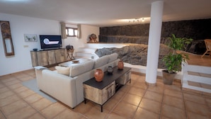 Un salon moderne avec un canapé, une table basse et un téléviseur. Il y a un mur en pierre et une plante dans le coin.