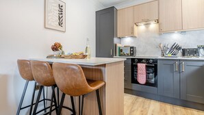 Une cuisine moderne avec un coin bar, des meubles en bois, un four à micro-ondes et un four encastré.