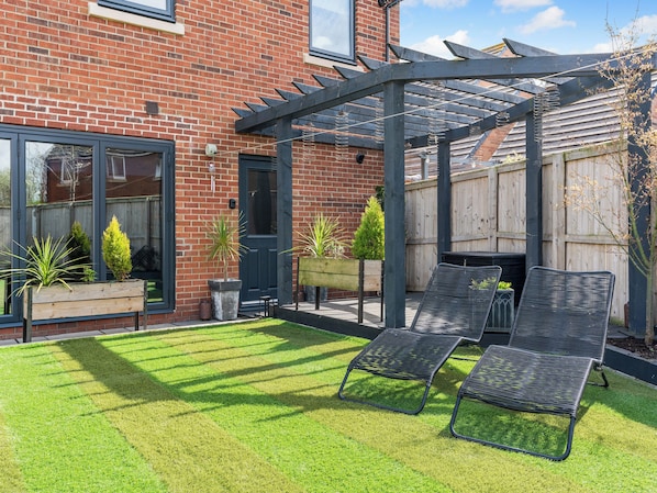 A patio with two lounge chairs, a wooden bench, and a pergola structure.
