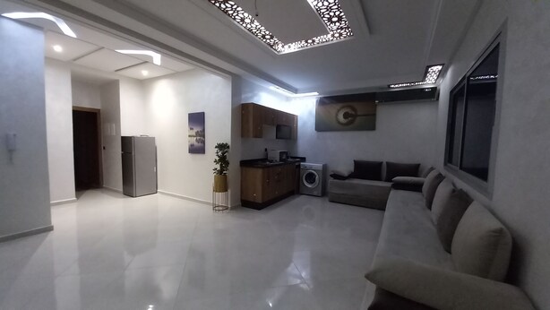 A modern living room with a flat-screen TV, a sofa, a washing machine, and a refrigerator. - Charming apartment in wonderful Fes with WiFi, AC (Fes)