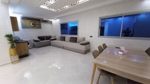 A modern living room with a sofa, a dining table, and a large window. - Charming apartment in wonderful Fes with WiFi, AC (Fes)