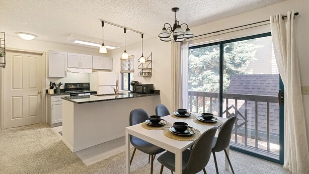 A modern kitchen with white cabinets, a dining area with a table set for four, and a large window with a view of trees. - DTC Apartment! Perfect for Your Extended Stay! (Greenwood Village)