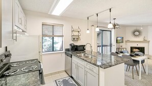 A modern kitchen with a built-in oven, microwave, and sink. There is a dining area with a table and chairs, and a fireplace in the background. - DTC Apartment! Perfect for Your Extended Stay! (Greenwood Village)