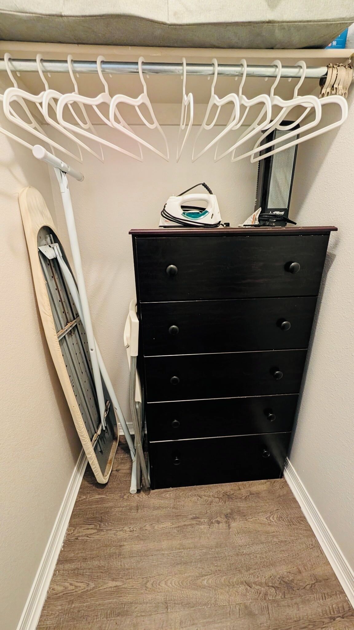 A corner room with a black dresser, a drying rack, and a window.