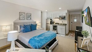 A bedroom with a bed, bedside lamps, and a nightstand. There is a kitchenette with a stove, microwave, and sink. A television is mounted on the wall. - DTC Studio w/ Kitchenette, Fast WiFi,Free Parking! (Greenwood Village)