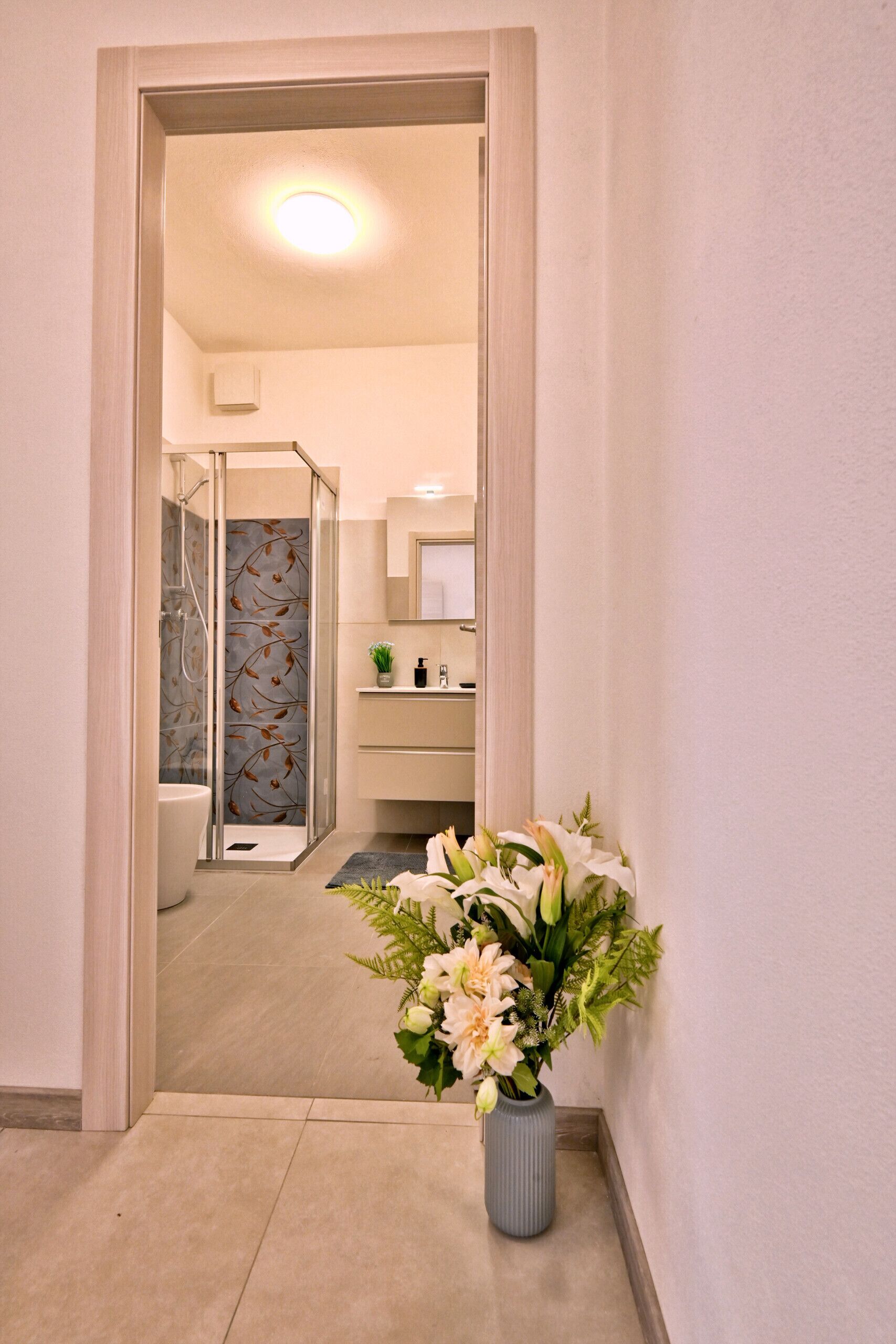 Ein Flur, der zu einem Badezimmer mit Dusche, Waschbecken und Spiegel führt.