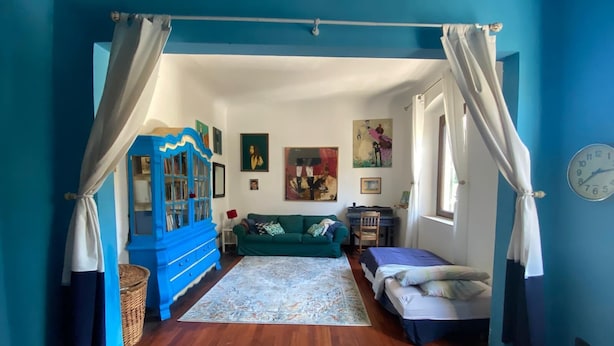 A room with a wooden floor, a green sofa, a blue cabinet, and a bed with a blue bedspread. - Charming 1 bedroom & sofa bed in a unique and quaint part of Florence. (Firenze)