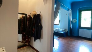 A room with a wooden floor, a bed with a white headboard, a window with curtains, and a coat rack with various jackets. - Charming 1 bedroom & sofa bed in a unique and quaint part of Florence. (Firenze)