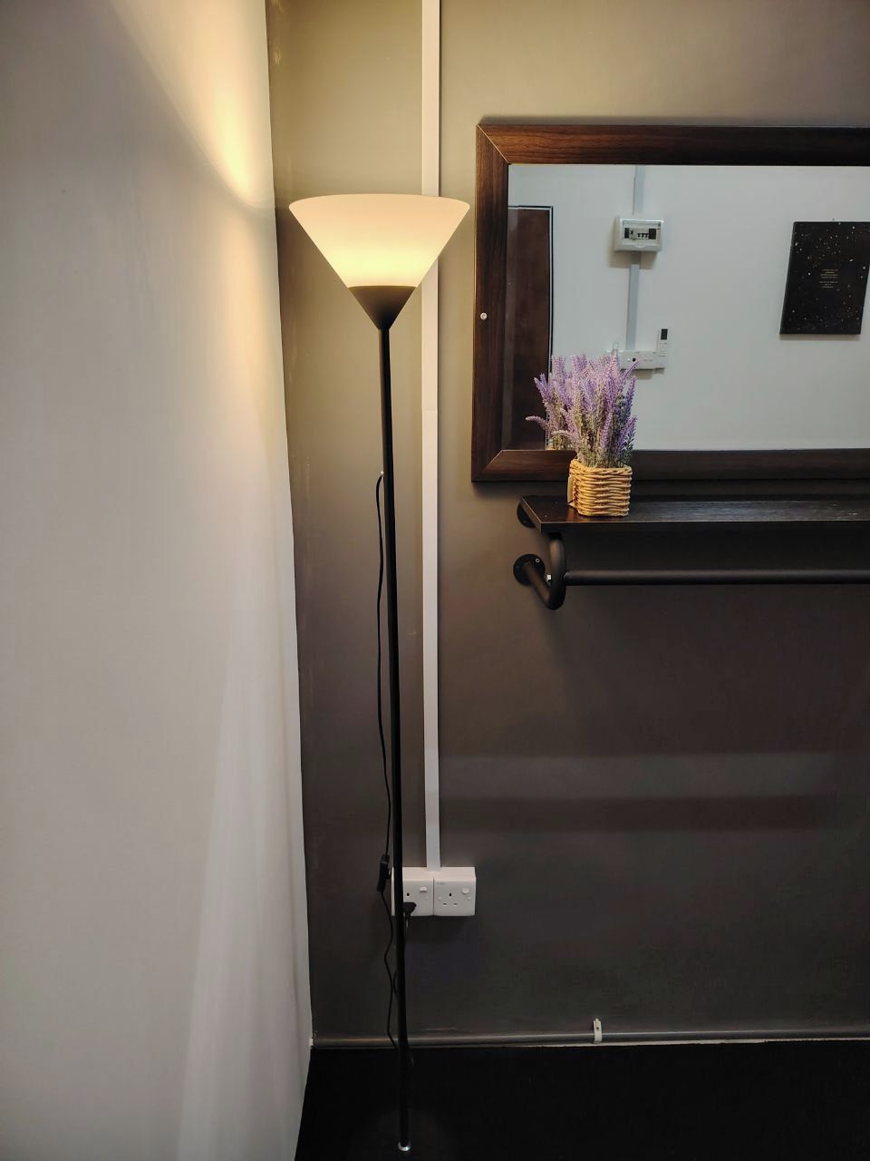 A modern room with a standing floor lamp, a mirror, and a shelf with a vase of flowers.