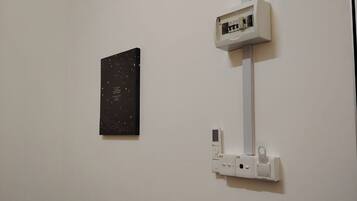 A room with a white wall, a black artwork, and a white electrical box.