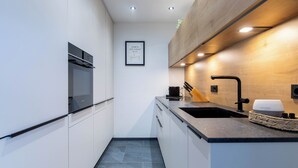 Eine schmale Küche mit weißen Schränken, einer schwarzen Arbeitsplatte und einer Wand in Holzoptik.