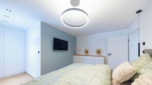 Ein modernes Schlafzimmer mit Bett, Fernseher, Kleiderschrank und Deckenleuchte.