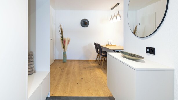 Ein modernes, minimalistisches Zimmer mit einem Holzesstisch, einer weißen Kommode und einem großen Spiegel.