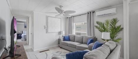 Un salon moderne avec un canapé gris, un ventilateur de plafond et une grande fenêtre avec des rideaux.