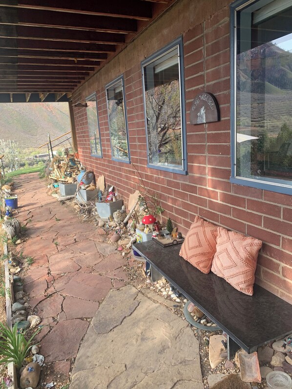 A covered patio with a brick wall, large windows, and a bench with cushions. - Very Private, Close to all Glenwood attractions, Pets welcome. 420 friendly! (Glenwood Springs)