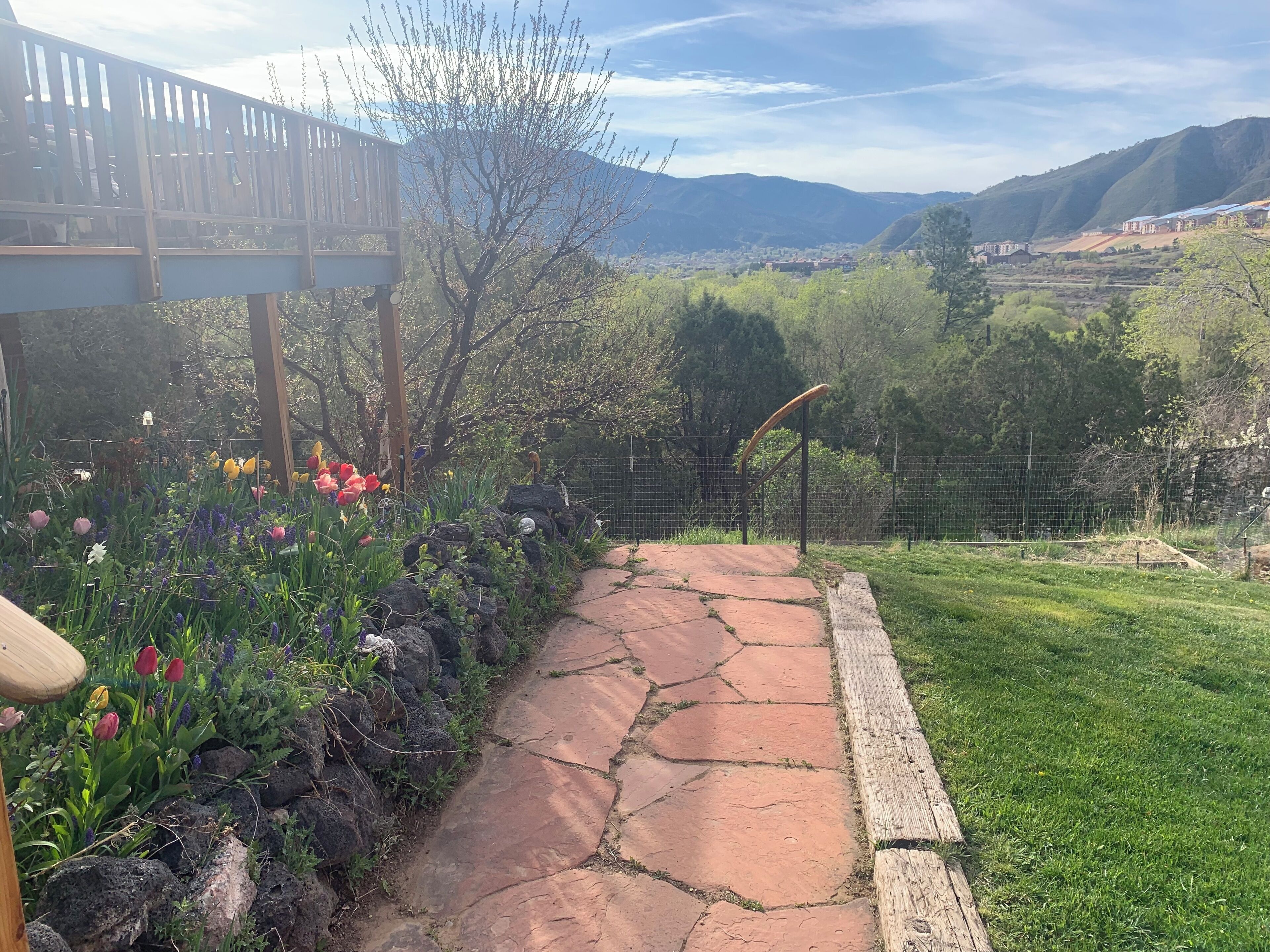 A garden pathway with a wooden deck and a view of a town and mountains in the background.