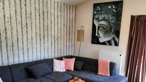 A modern living room with a sectional sofa, a small wooden side table, and a large abstract painting on the wall. - Luxury, space, comfort and nature for two: The Veluwe Happy Together! (Epe)
