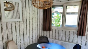 A dining area with a round table, four chairs, a wicker pendant light, a window with curtains, and a radiator. - Luxury, space, comfort and nature for two: The Veluwe Happy Together! (Epe)